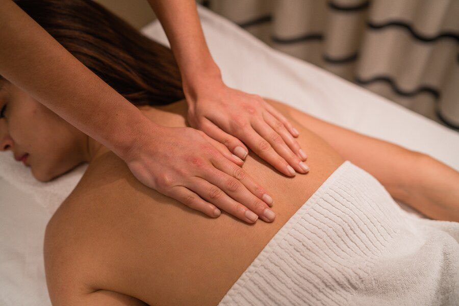 Femme recevant un massage sur le dos, avec des mains visibles sur sa peau.