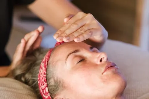 Femme recevant un soin relaxant, la main sur le front, les yeux fermés.