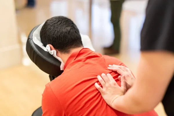 Une personne reçoit un massage sur une chaise, vêtue d'un polo rouge.