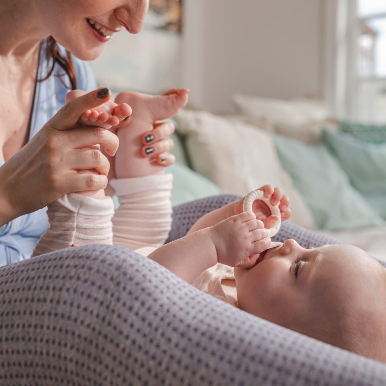 Photographie douce et naturelle d'une maman massant les pieds de son bébé endormi. Ambiance cocon avec touches de Vert Sauge et Terracotta à