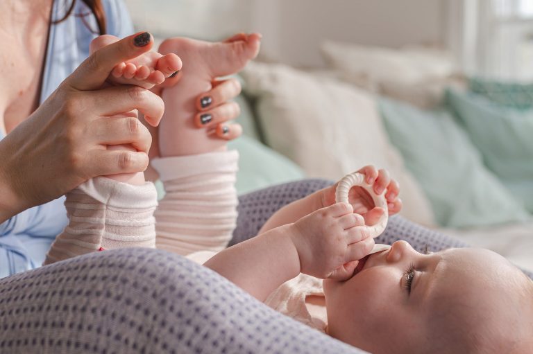Photographie douce et naturelle d'une maman massant les pieds de son bébé endormi. Ambiance cocon avec touches de Vert Sauge et Terracotta à
